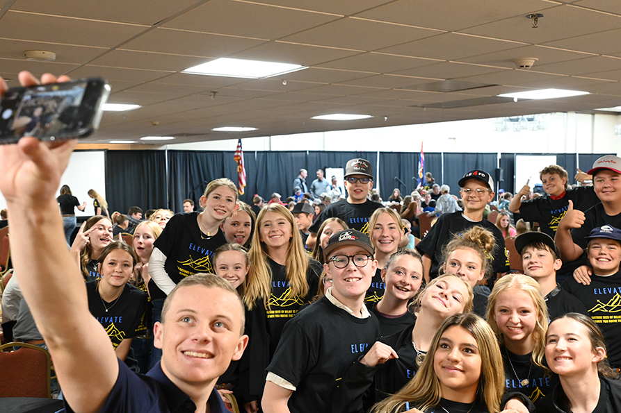 Middle school students in matching black ‘Elevate’ shirts gather for a group selfie at an indoor FFA event.