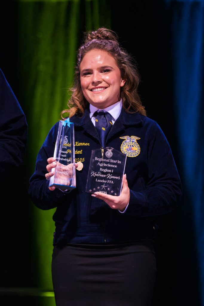 A Wyoming FFA member from Lander FFA holds Regional Star in Agriscience award plaques on stage at state convention.