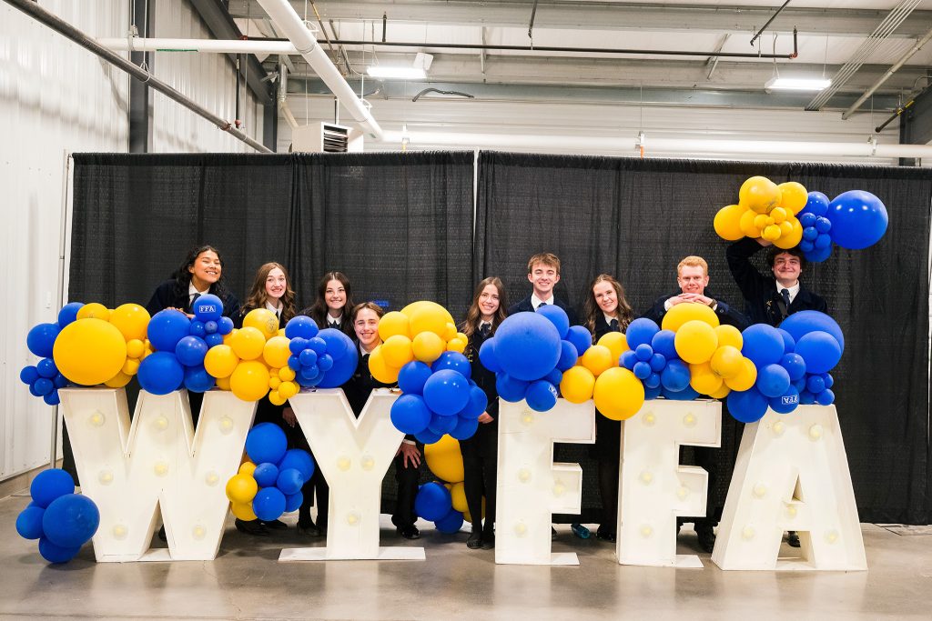 State officers for FFA standing behind white letters that spell FFA and blue and gold balloons.