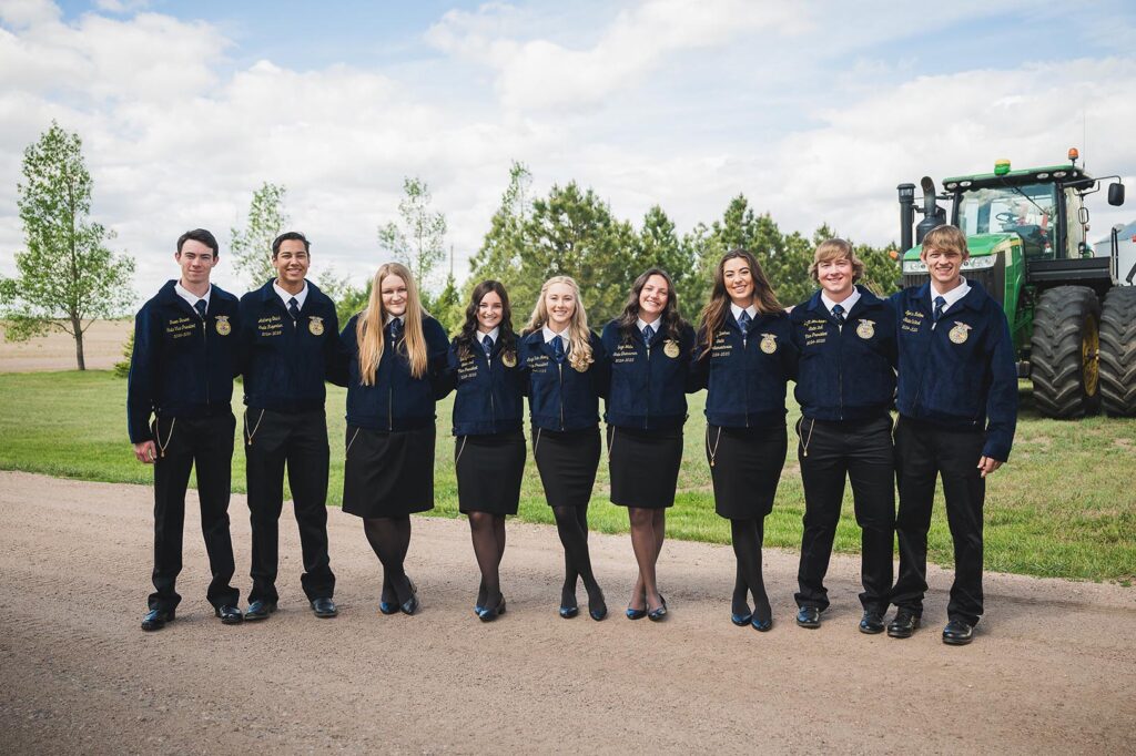 nine student officers in ffa jackets standing in front of a tractor